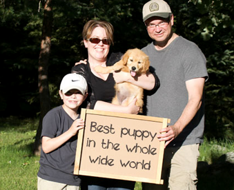 outdoor photo of family holding a golden retriever puppy and a Gotcha Day sign