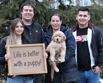 outdoor photo of family holding a golden retriever puppy and a Gotcha Day sign