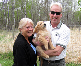 outdoor photo of man and woman with a golden retriever puppy