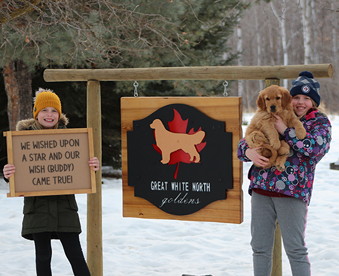 outdoor winter photo of a two girls holding a golden retriever puppy and a Gotcha Day sign