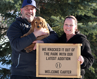 outdoor winter photo of a couple holding a golden retriever puppy and a Gotcha Day sign