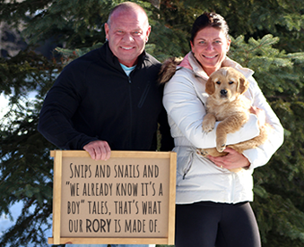 outdoor winter photo of a couple holding a golden retriever puppy and a Gotcha Day sign