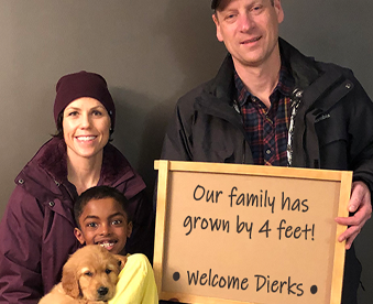 indoor photo of a family holding a golden retriever puppy and a Gotcha Day sign