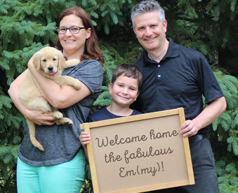 outdoor photo of a family holding a golden retriever puppy and a Gotcha Day sign