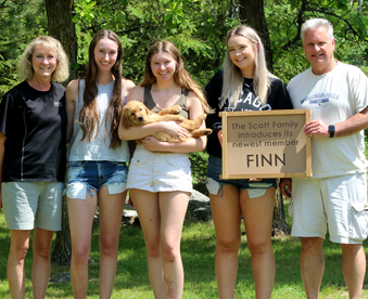 outdoor photo of a family holding a golden retriever puppy and a Gotcha Day sign