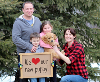 outdoor photo of family holding a golden retriever puppy and a Gotcha Day sign