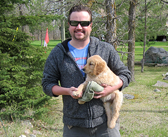 outdoor photo of man holding a golden retriever puppy