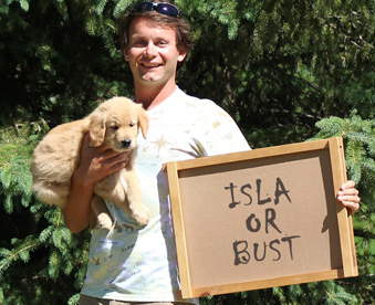 outdoor photo of a man holding a golden retriever puppy and a Gotcha Day sign