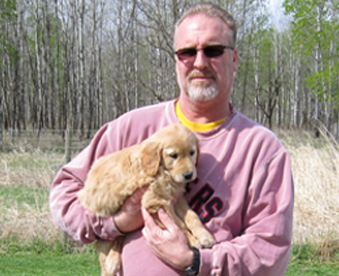 outdoor photo of man holding a golden retriever puppy