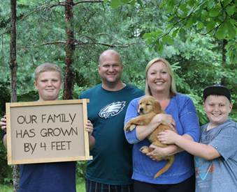 outdoor photo of family holding a golden retriever puppy and a Gotcha Day sign