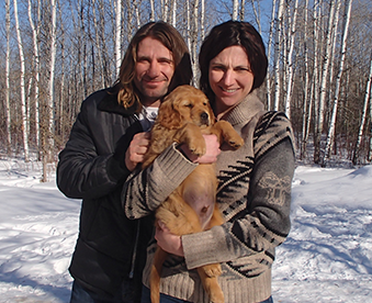 outdoor photo of a couple holding a golden retriever puppy