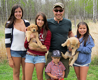 outdoor photo of family with two golden retriever puppies