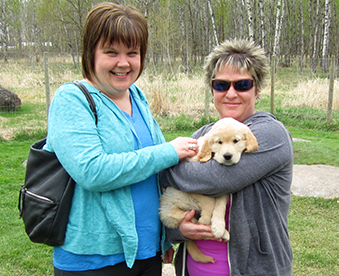 outdoor photo of two women with a golden retriever puppy