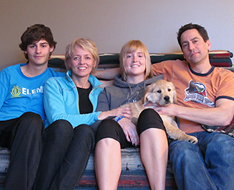 photo of a family sitting on sofa with their golden retriever puppy