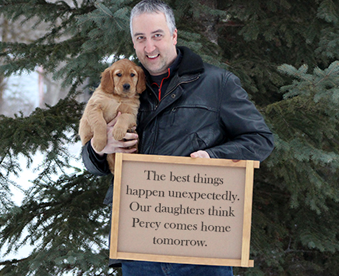 outdoor winter photo of a man holding a golden retriever puppy and a Gotcha Day sign