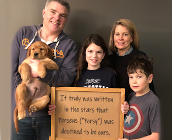 indoor photo of a family holding a golden retriever puppy and a Gotcha Day sign