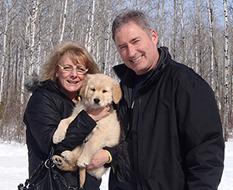 outdoor photo of a couple holding a golden retriever puppy