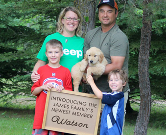 outdoor photo of family holding a golden retriever puppy and a Gotcha Day sign