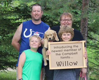 outdoor photo of family holding a golden retriever puppy and a Gotcha Day sign