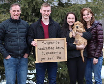 outdoor photo of family holding a golden retriever puppy and a Gotcha Day sign