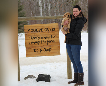 outdoor winter photo of a woman holding a golden retriever puppy and a Gotcha Day sign