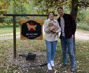 outdoor autumn photo of a couple holding a golden retriever puppy and a Gotcha Day sign