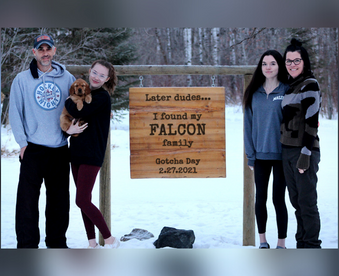 outdoor winter photo of a family holding a golden retriever puppy and a Gotcha Day sign