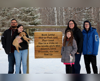 outdoor winter photo of a family holding a golden retriever puppy and a Gotcha Day sign