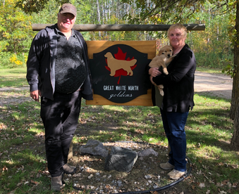 outdoor autumn photo of a couple holding a golden retriever puppy and a Gotcha Day sign