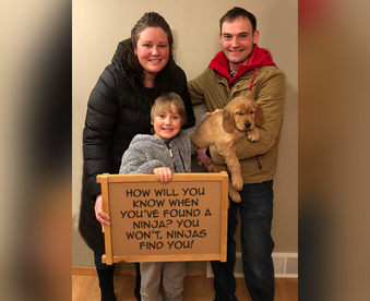 photo of a family of three holding a golden retriever puppy and a Gotcha Day sign