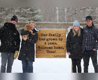 outdoor winter photo of a family holding a golden retriever puppy and a Gotcha Day sign