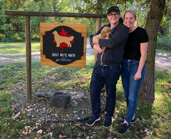 outdoor autumn photo of a couple holding a golden retriever puppy and a Gotcha Day sign