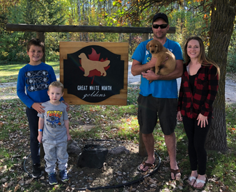 outdoor autumn photo of a family holding a golden retriever puppy and a Gotcha Day sign