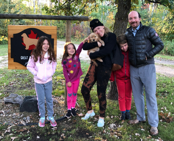 outdoor autumn photo of a family holding a golden retriever puppy and a Gotcha Day sign